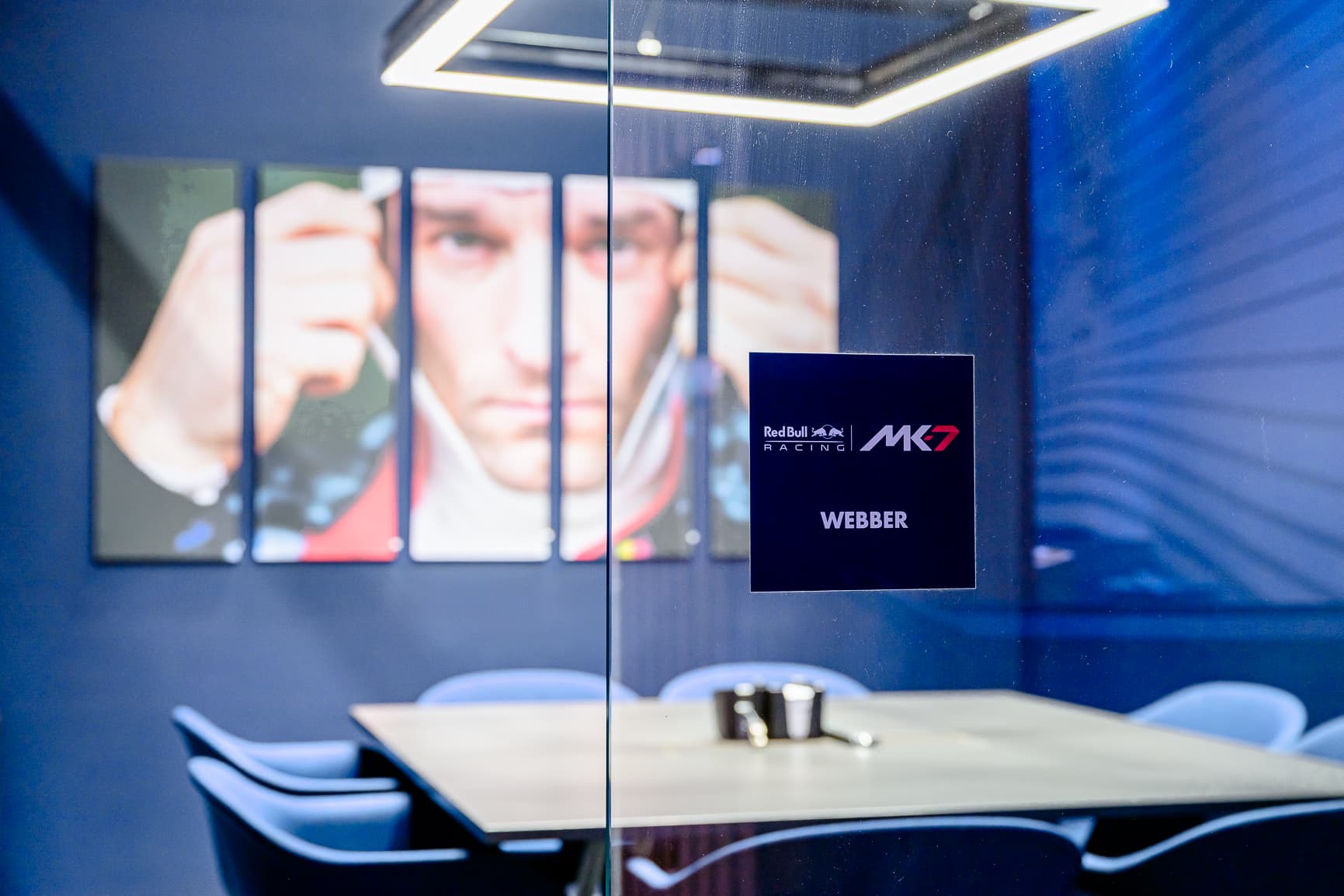 Glass-walled meeting room with "WEBBER" sign, blue chairs, a table with cups, and a large portrait on the wall.