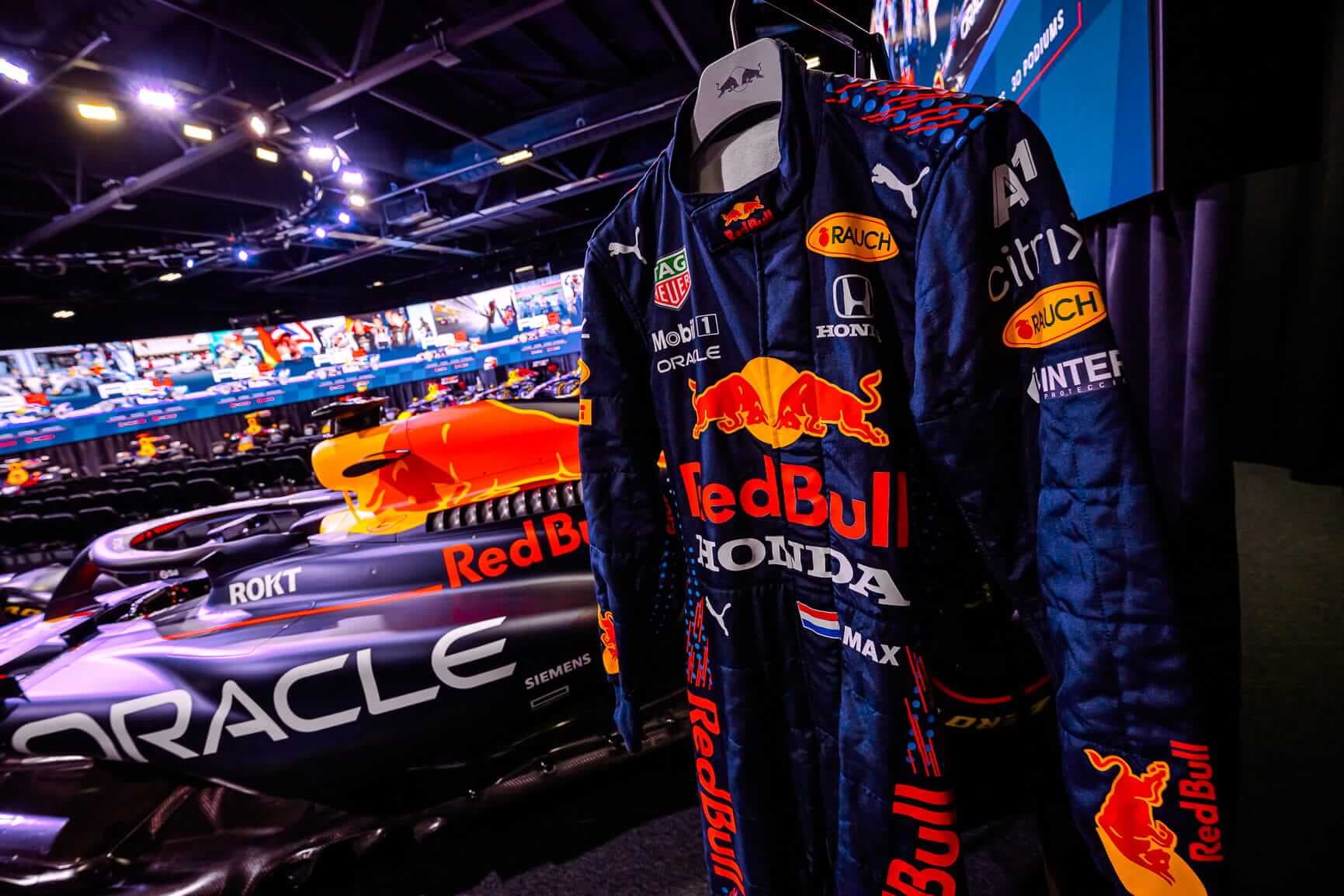 A race suit at the front of the picture with a background of race cars and a digital screen